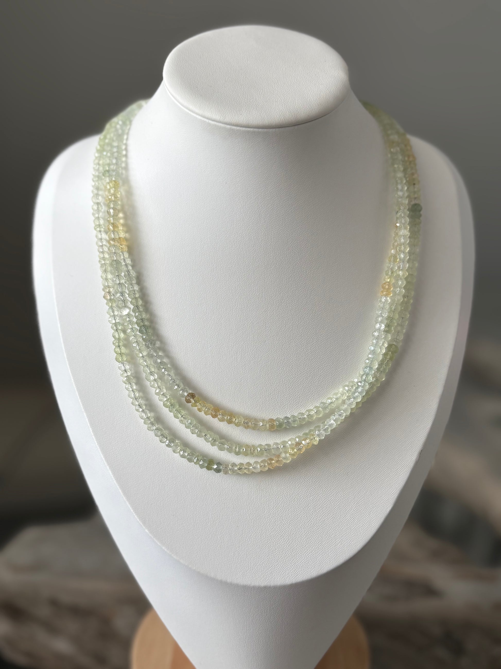 Long Prehnite Necklace with three strands of faceted light green and yellow beads on a white bust