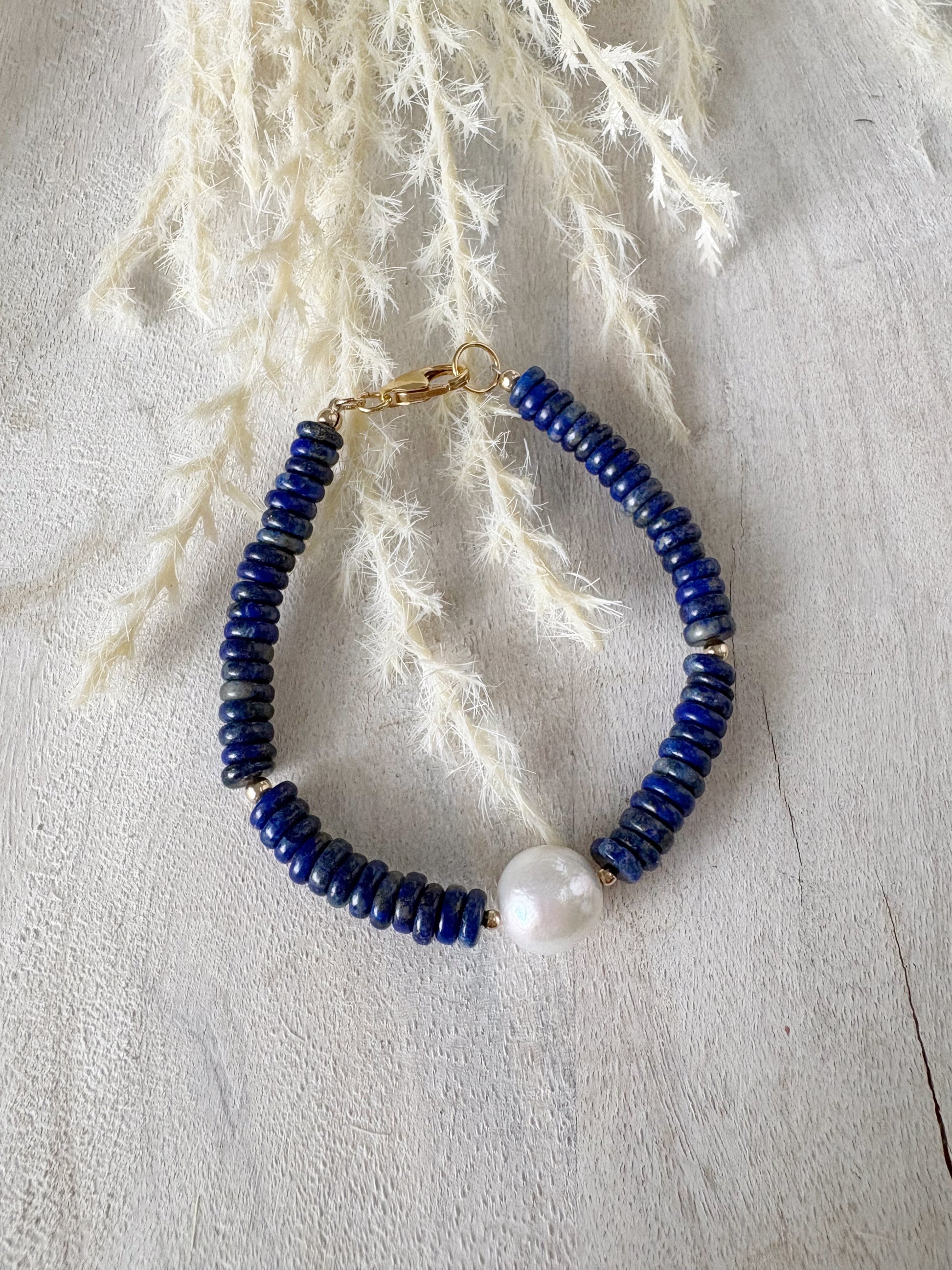 Lapis and Pearl Bracelet with blue lapis beads and a single white pearl on a light wooden surface
