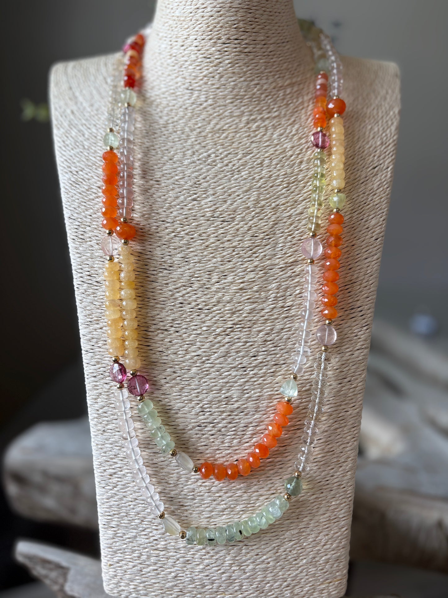Multi Gemstone Necklace with orange, yellow, pink, and green beads on a textured display